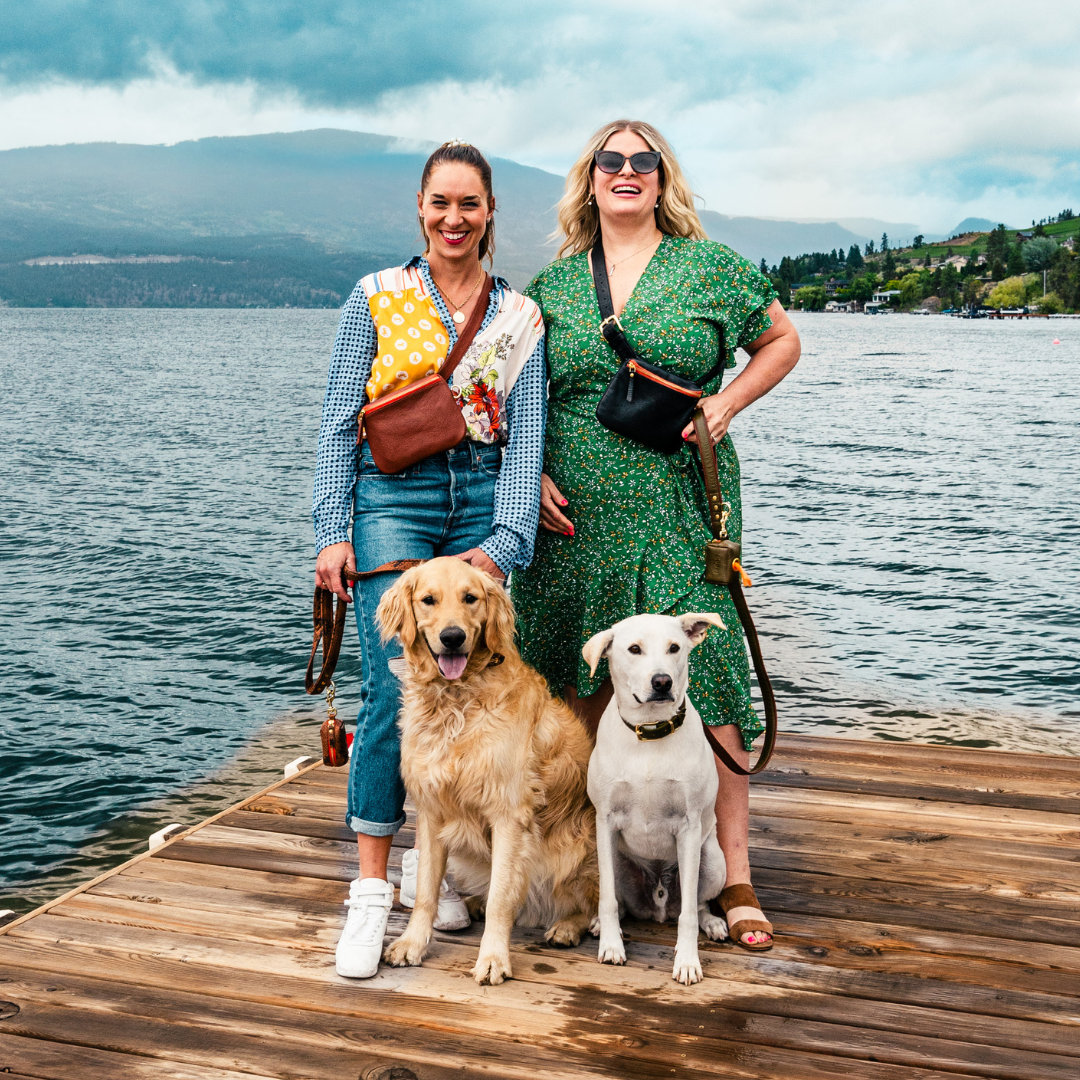 Two women and their dogs on a dock with Le Fanny pack made from genuine leather and all brass hardware.